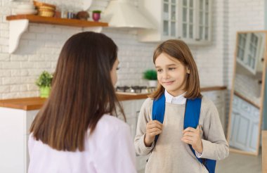 Mother and son prepare in morning before first day of school, child and mum standing together in home kitchen. Schoolboy with backpack looking at mom with love and smile. Learning start concept