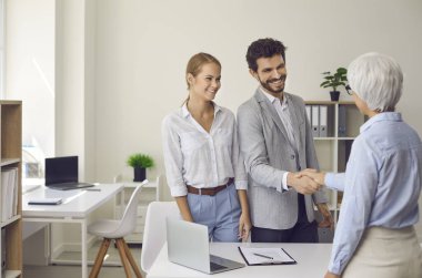 Happy married couple shaking hands with a female lawyer, realtor or financial advisor. Man and woman at a reception at an insurance broker or bank employee. Concept of business ethics and trust.