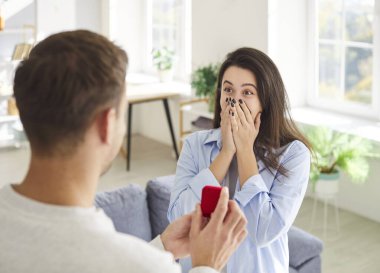 Marry me proposing, man holding red box with marriage engagement ring, proposal to loving surprised woman, girlfriend covering face, lover offering romantic Valentines day gift, feeling surprise 