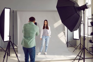 Male photographer shooting model in studio with with professional equipment. Beautiful young model posing for photo, rare view of male photographer taking pictures with digital camera