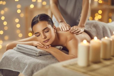 Young woman having back massage in beauty spa salon. Serene beautiful relaxed woman lying on couch with closed eyes receiving and enjoying relaxing massage. Beauty treatment, body care