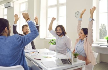 Overjoyed diverse businesspeople raise hands celebrate shared business success or goal achievement in office. Smiling multiethnic employees engaged in teambuilding activity. Teamwork concept.