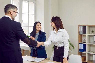 We hire you. Hiring committee shakes mans hand, welcoming him as new member of business team. Two satisfied women together with man in suit seal deal with handshake in office. Recruitment concept.