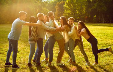 Full length portrait of a funny happy overjoyed students friends having fun in nature in the summer park pushing each other enjoying time together at sunny day. Team building and friendship concept.