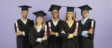 Diverse group of happy proud mixed race university students in graduate mortarboard hats and robes, with diploma scrolls standing arms crossed on purple color background. Banner. Graduation concept