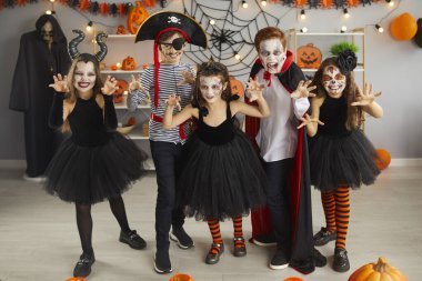 Portrait of group of children in creative costumes with scared faces at Halloween party. Little boys and girls with spooky makeup standing in room decorated for Halloween looking scared at camera.