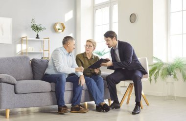 Senior couple of clients holding a meeting with a consultant or agent at home. Discussing financial contract, insurance options, or investment matters in a comfortable domestic setting.