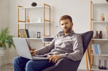 Portrait of a young successful businessman at home. Relaxed young business man with a modern laptop computer on his lap lounging in a comfortable armchair and looking at the camera