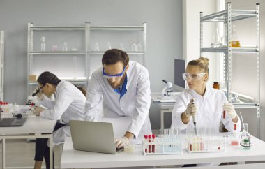 Scientists are doing important research. A woman holds a test tube, a man works at a laptop. Teamwork of professionals. Professional teamwork of scientists