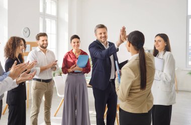 Overjoyed office businesspeople give high five, engaged in teambuilding activity at meeting, happy diverse colleagues clap hands to celebrate common shared victory or win at team briefing, success 
