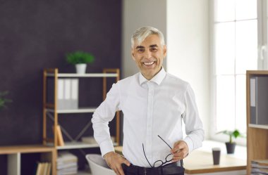 Portrait in the office of a successful happy senior European businessman or manager. Gray-haired experienced manager working in the office of a modern business center smiles and looks at the camera.