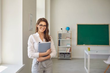 Okula dönelim. Okulda gözlüklü, not defteriyle ayakta duran pozitif öğretmen kadın. Ebeveynlik eğitimi almak.