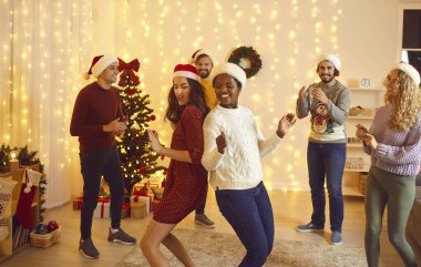 Happy diverse friends dance have fun celebrating Christmas together. Smiling multiethnic young people enjoy home party involved in New Year celebration at home. Winter holiday, friendship.