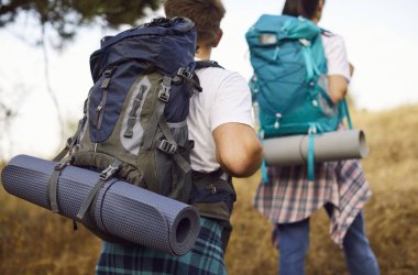 Hikers couple with backpacks on forest trail. Close view of packs and mats as they climb hillside, enjoying travel adventure, trekking, and nature outdoors. Outdoor couple hiking, travel theme.