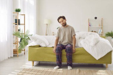 Adam pazartesi sabahı çok erken bir saatte uykudan kalkmaya çalışıyor. Uykulu, tişörtlü ve pijama pantolonlu yorgun bir adam evdeki koltukta gözleri kapalı oturuyor.