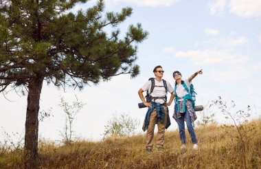 Couple hikers, backpackers explore forest together outdoors. They stop on the hillside, enjoying nature as they travel, turning trekking into adventure. Concept: travel, love, outdoor adventure.
