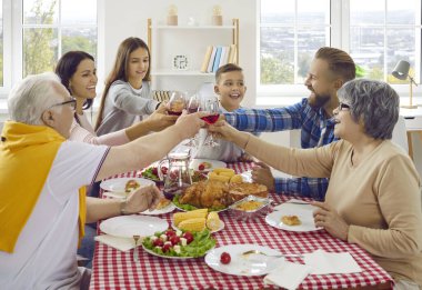 Family toast. Joyful friendly multigenerational family clinking wine glasses during Thanksgiving celebration. Family members of different ages are sitting together at home at festive table.
