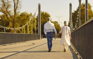 Senior couple walking hand in hand shows love, unity, and lifelong connection. Peaceful autumn walk promotes wellbeing, relaxation, and emotional health. A moment of togetherness and harmony.