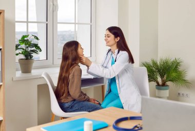 Kadın gülümseyen çocuk doktoru sağlık kliniğinde küçük kız hastaların boğazını muayene ediyor. Doktor kadın otolarolog muayenehanedeki hasta bir çocuğun ağız boşluğunu muayene ediyor..