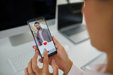 Bringing together people of different professions and walks of life through online dating apps or websites. Close up businesswoman looking at phone display gives like to photo of handsome young farmer