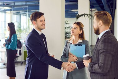 Handshake between professional business people seals an agreement during an office meeting. The scene reflects a successful deal, partnership, and teamwork within a corporate community.