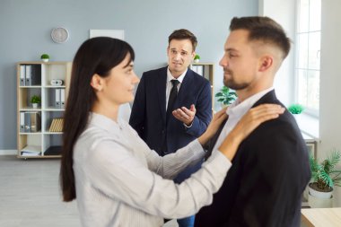 Indoors, woman holds man by shoulders while another man looks on, reflecting tense love triangle with cheating and hidden affair. Scene portrays deception, betrayal and emotional conflict.