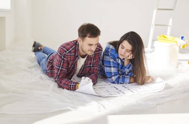 Happy young married couple amuse looking at repair project on paper blueprints, planning future work, discussion, architectural and interior design ideas, feeling positive after moving new flat