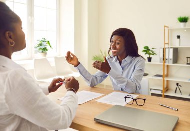 Ofisteki heyecanlı, gülümseyen iş kadınları. Kadın Afro-Amerikan şirket çalışanları çalışma masasında oturuyor, konuşuyor ve tartışıyorlar, yeni projeler ya da girişimler düşünüyorlar..