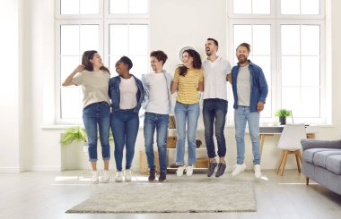 Happy, joyful friends having fun at a small gathering at home. Diverse group of different overjoyed, cheerful young mixed race people jumping all together in a modern white living room interior