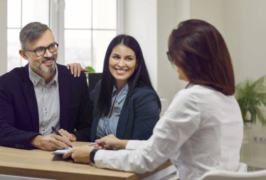 Portrait of an attractive, happy man and two beautiful, young women talking in a business setting, sitting at a desk in the office. Familiarization and signing of documents during working hours.