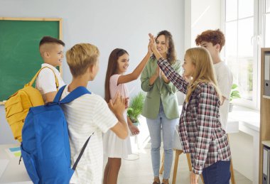Classmates meeting after summer holidays. Happy smiling school children giving high five each other in the classroom with their friendly woman teacher. Back to school and education concept.