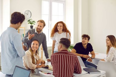Friendly clever male teacher discusses with students explaining material during lesson on courses. Smiling male and female university students talking to teacher in classroom. Education concept.