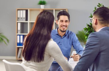 Friendly, smiling professional real estate agent, bank manager, financial adviser or loan broker having a business meeting with a young family couple in the office