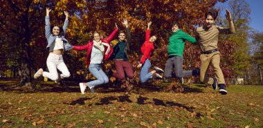 Group of a young friends walking in the autumn park. Happy caucasian people girls and boys having fun, jumping outdoors. Smiling students in casual clothes spending time together. Banner.