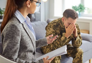 Crying young soldier man dressed in military uniform seeks support during professional psychological therapy session with female psychologist. Mental health care for veterans, recovery, reintegration