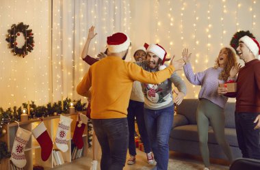 Overjoyed diverse international friends hug enjoy New Year celebration at home. Happy multiethnic young people have fun gather reunite at Christmas party, celebrate winter holidays together.