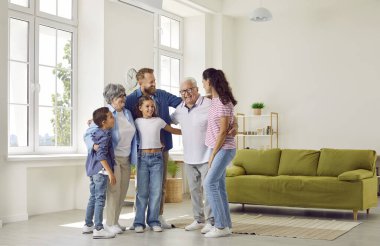 Happy extended multigenerational family having fun at home. Cheerful, joyful grandparents, grandchildren and their parents hugging all together in light spacious white living room with green sofa