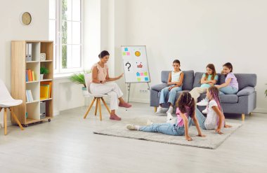 Happy smiling school psychologist behaviour specialist and group of kid children friend girls sit in office classroom after class discussing conflict misunderstanding situation and solution to problem
