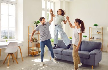Happy laughing family having fun with a child girl in the living room at home. Portrait of young couple parents playing and spending time together with their daughter. Family time concept.