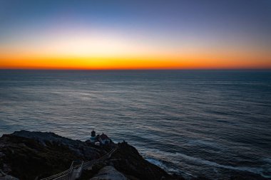 Point Reyes Deniz Feneri 'nin gün batımındaki uzak görüntüsü su arka planında. Point Reyes National Seashore, Marin County, California, ABD.