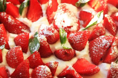 Krem şantili bir kekin içinde çilek dilimleri. Nane yapraklı vinç planıyla kesilmiş olgun çilek parçaları.