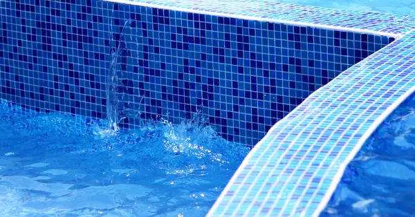 Water in the pool. Water flowing from the pool. Water is poured from the pool into another pool. Water in the pool on the background of blue ceramic tiles