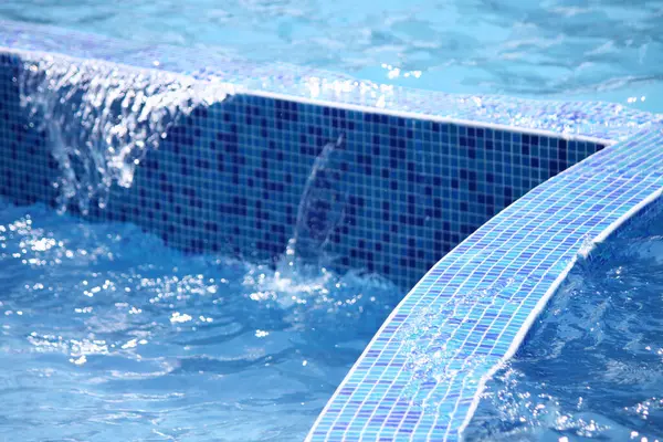 Water in the pool. Water flowing from the pool. Water is poured from the pool into another pool. Water in the pool on the background of blue ceramic tiles