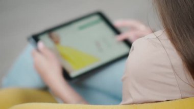 İnternetten alışveriş için dijital tablet kullanan bir kız. Ekranın bulanık görüntüsü ve kıyafetlerle siteye bakan genç bir kadın.
