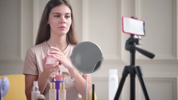 漂亮的女孩在做一个美容产品的概览 年轻的博客作者用三脚架上的智能手机拍摄博客 — 图库视频影像