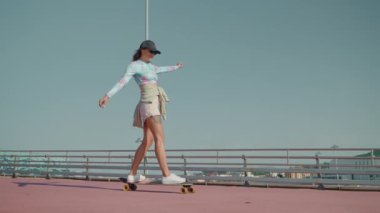 Yavaş çekim, neşeli ve kaygısız kızın hareket eden kaykayın üzerinde dengede durması. Aktif olarak boş zamanın tadını çıkarıyorum.