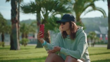 Spor görünümlü genç bir kadın Green Park 'ta online video konuşması yapıyor. Fikirlerini ve sorunlarını bir arkadaşıyla paylaşan bir kız.
