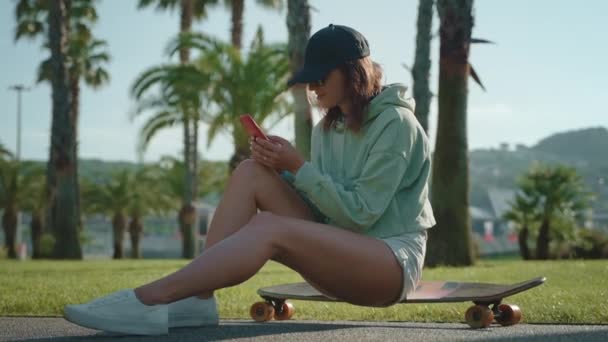 Αθλητικό Κορίτσι Στυλ Κάθεται Στο Longboard Και Γραπτών Μηνυμάτων Smartphone — Αρχείο Βίντεο