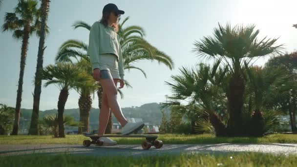 Ung Sportskvinne Hettegenser Shorts Skal Stå Skateboard Blant Grønne Håndflatene – stockvideo