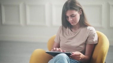 Evde tablet bilgisayar kullanan güzel bir kız. Ekranda görüntüyü yakınlaştırıyor. Fotoğraflara bakmak, sosyal medyaya bakmak ya da online alışveriş